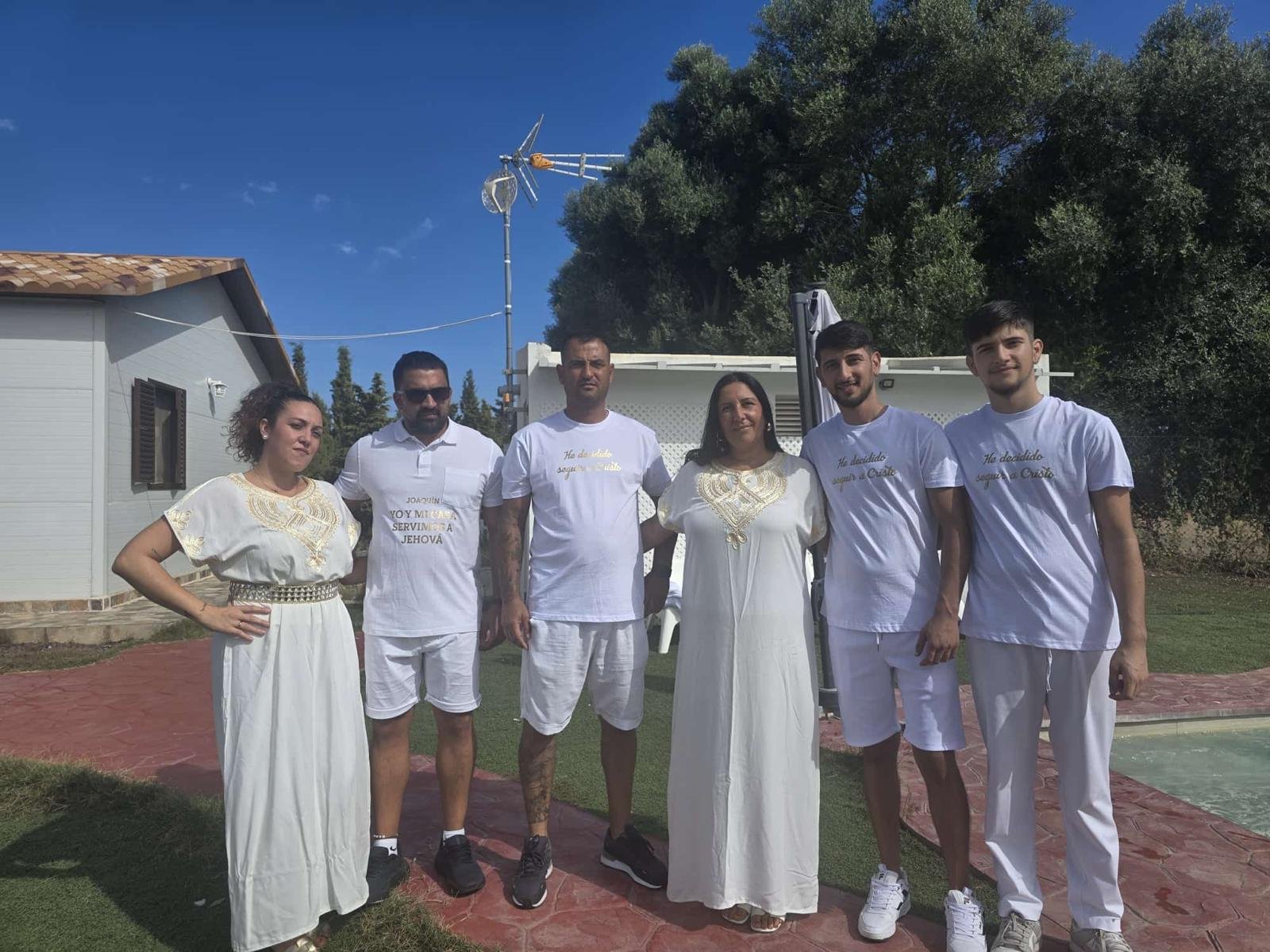 El grupo de bautismo posando junto a la casa y la piscina del jardín, todos vestidos de blanco