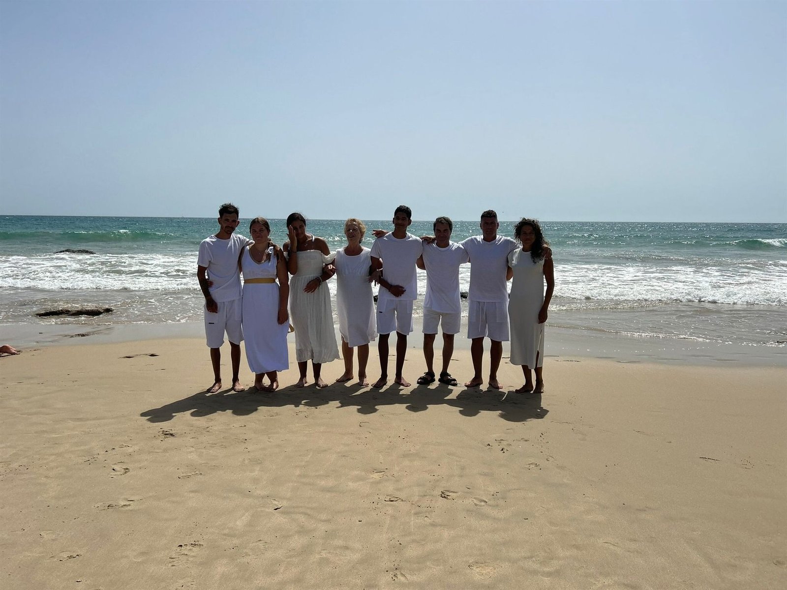 El grupo de bautismo posando en la orilla de la playa, vestidos de blanco, con el mar de fondo