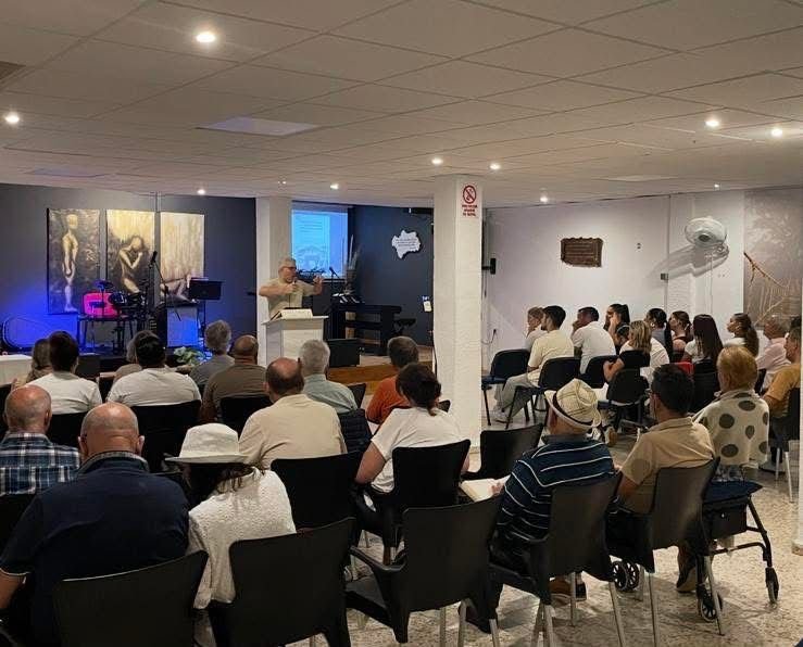 Interior del templo durante un culto: el pastor predica de pie tras el atril ante la congregación sentada